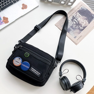 Detail of black canvas messenger bag with mesh pocket and trendy patches on white desk