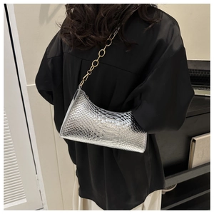 Close-up of silver snakeskin texture baguette bag with golden chain strap on a model