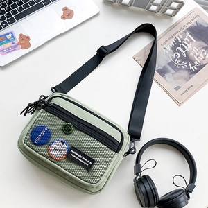 Close-up of light green canvas crossbody bag with mesh pocket and decorative badges