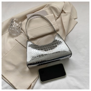 Close-up of silver baguette bag with crocodile texture on a beige suit background