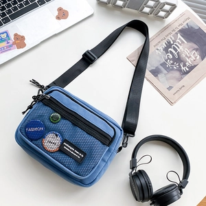 Detail of blue canvas messenger bag with mesh pocket and badges on a desktop set