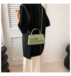 Détail du sac à main vert clair gaufré crocodile avec boucle dorée porté par un mannequin