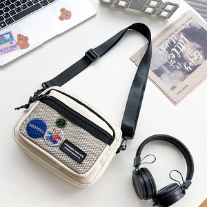 Close-up of off-white canvas crossbody bag with mesh pocket and black nylon shoulder strap