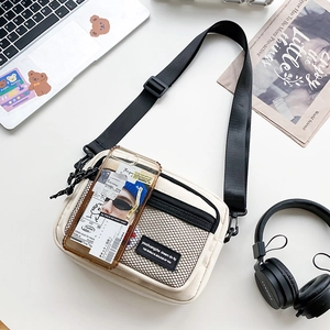 Close-up of cream canvas messenger bag featuring black mesh pocket and adjustable strap