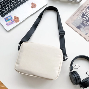 Detail of minimalist beige canvas crossbody bag with black adjustable strap and laptop