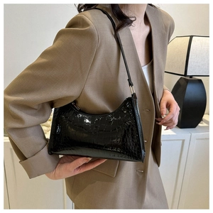 Close-up of black crocodile pattern glossy shoulder bag worn by model in soft indoor light