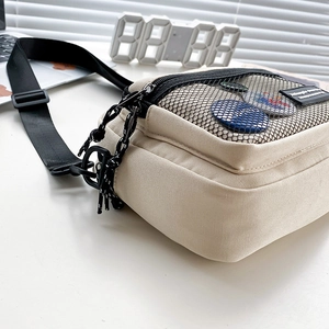 Detail view of cream canvas crossbody bag with mesh pocket and black adjustable strap