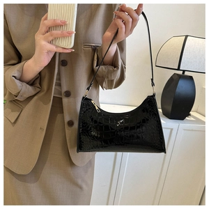 Detail of black faux leather baguette bag with crocodile pattern worn with a brown blazer