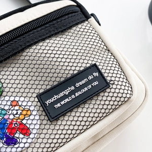 Detail of canvas crossbody bag featuring black nylon mesh pocket and logo patch