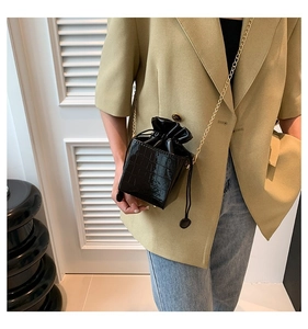 Dettaglio di una borsa a secchiello nera coccodrillo con catena d'oro e chiusura a coulisse