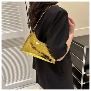 Close-up of golden faux-leather shoulder bag with crocodile texture worn by a model