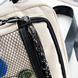 Detail view of canvas crossbody bag with mesh pocket and decorative badges