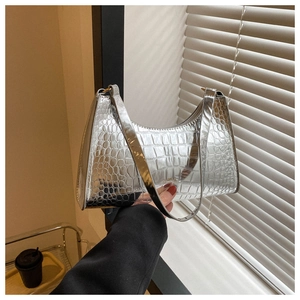 Close-up of silver crescent underarm bag with glossy crocodile texture and metal finish