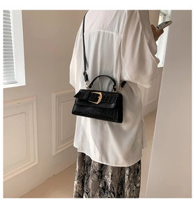 Détail d'un sac à main noir à motif crocodile avec fermoir doré porté par un mannequin