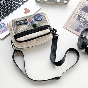 Detail of off-white canvas crossbody bag with mesh pocket and badges on a white desk