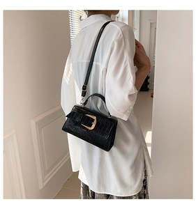 Détail d'un sac à main noir texture crocodile avec boucle dorée porté à l'épaule