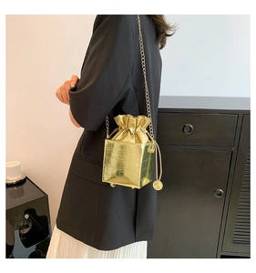 Dettaglio della mini borsa a secchiello oro lucido con trama coccodrillo e catena dorata