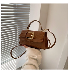 Détail d'un sac à main marron motif crocodile avec fermoir doré et poignée supérieure tenu