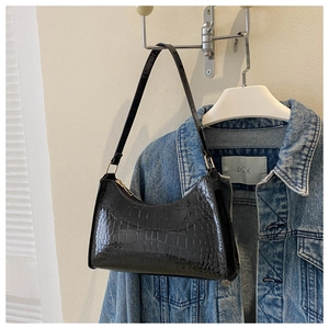 Detail of black patent leather baguette bag with crocodile texture on denim jacket
