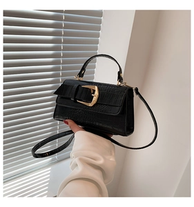 Détail d'un sac à main noir à texture crocodile avec boucle dorée et poignée renforcée
