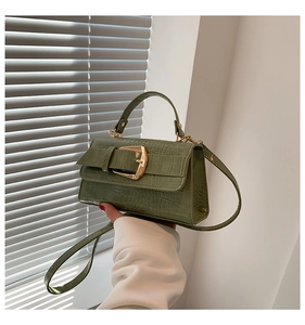 Détail d'un sac à main vert avocat à motif crocodile avec boucle dorée et poignée ronde