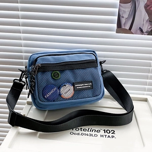 Detail of blue canvas messenger bag featuring a black mesh pocket and fashion patches