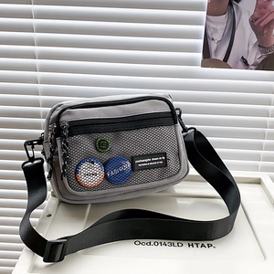 Detail view of a gray canvas messenger bag featuring a front mesh pocket and stylish badges