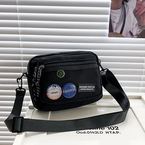 Close-up of black canvas messenger bag featuring mesh front pocket and decorative pins