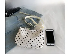 Grootte vergelijking van een witte nylon schoudertas met stippen naast een smartphone