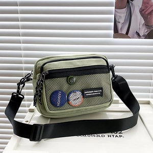 Detail of green canvas crossbody bag featuring black mesh pocket and trendy badges