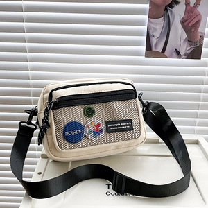 Close-up of beige canvas crossbody bag featuring front mesh pocket and creative badges