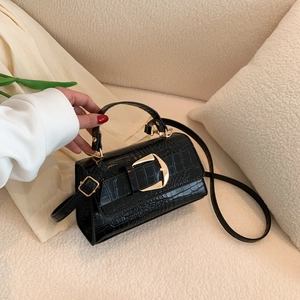 Sac à main noir avec motif crocodile et boucle dorée sur un canapé beige élégant