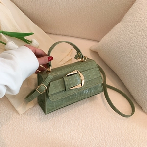 Sac à main vert effet crocodile avec boucle dorée posé sur un canapé beige
