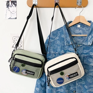 Detail of canvas messenger bags in mint green and beige with mesh pocket and badges