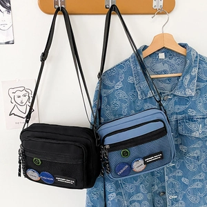 Detail of canvas messenger bag featuring a mesh pocket and fashion badge decorations