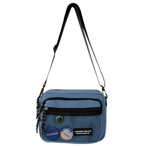 Close-up of blue canvas crossbody bag with mesh pocket, trend badges, and nylon strap