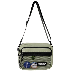 Detail of light green canvas crossbody bag featuring front mesh pocket and brand patch