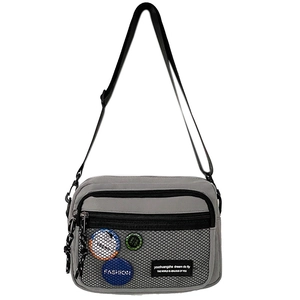 Detail view of grey canvas crossbody bag with mesh pocket and decorative badges