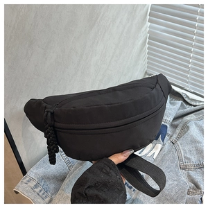 Detail of a minimalist black nylon waist bag with a woven pull zipper and wide strap