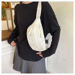Close-up of beige nylon crossbody bag with dual zippers and woven pulls on a model