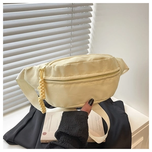 Detail of light yellow nylon waist bag featuring zip pockets and woven cord tassels