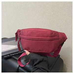 Detail of burgundy nylon waist bag featuring a woven zipper pull and adjustable strap