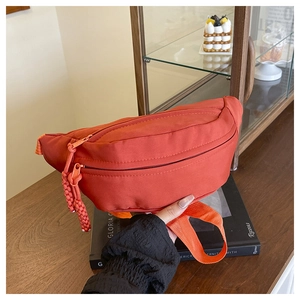 Detail view of bright orange nylon waist bag with textured fabric and woven zip puller