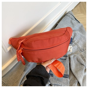 Close-up of a brick red nylon crescent waist bag with a woven zipper puller detail