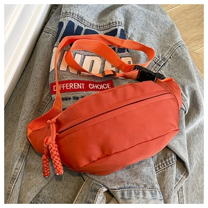 Close-up of orange nylon crossbody chest bag with adjustable strap and buckle on denim jacket