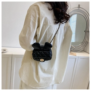 Rear view of a model wearing a mini black quilted crossbody bag with rabbit ears and chain