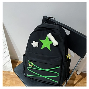 Detail of black backpack with green star patch, cross drawstrings and plush charms