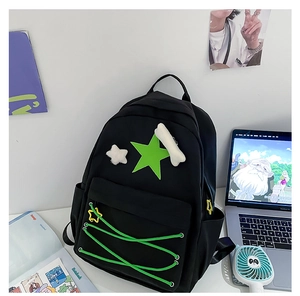 Detail view of black nylon backpack with green star patch and plush charms on a white desk