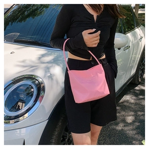 Pink nylon shoulder bag with embossed text detail shown in a stylish outdoor scene