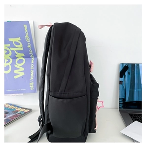 Side view of black nylon backpack featuring a pink star charm and functional side pocket